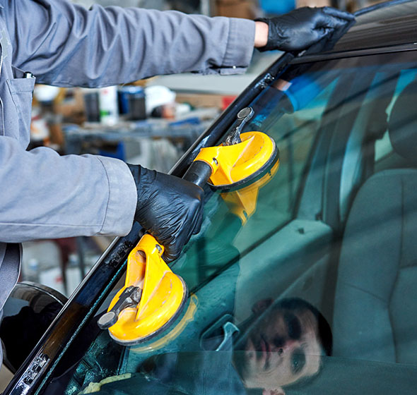 A technician in blue-sleeves holding a windshield replacement tool on a pristine new windshield